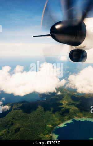 Propeller aircraft wing over tropical islands. Aerial view of airplane flying above shade clouds and sky Stock Photo