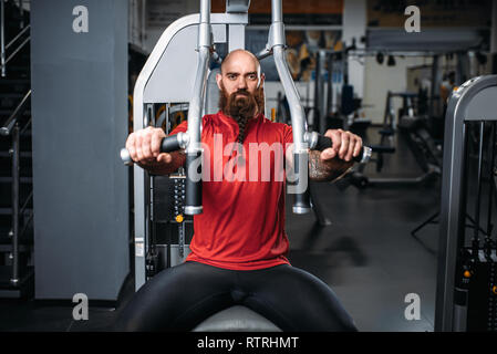 Muscular athlete on exercise machine in gym. Bearded man on workout in sport club Stock Photo