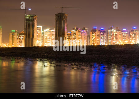 A beautiful shot of the city of Netanya in Israel during the night. bright city lights reflected off the water on a beach. Stock Photo