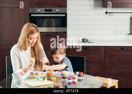 happy blonde mother and four-year old son making homemade Easter eggs, enjoying leisure time spent together at home. Family celebrating Easter. Parent Stock Photo
