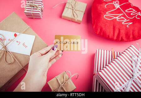 Buying presents for Valentines day with a gold card. Gift boxes and heart pillow on pink background Stock Photo
