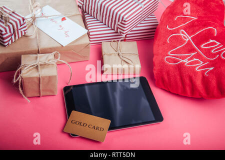 Buying presents for Valentines day with a gold card. Gift boxes and heart pillow on pink background Stock Photo
