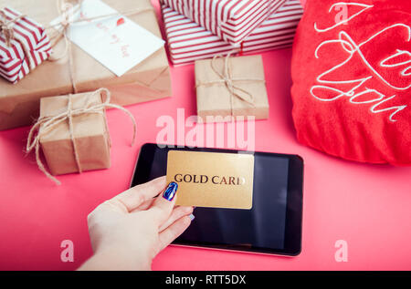 Buying presents for Valentines day with a gold card. Gift boxes and heart pillow on pink background Stock Photo