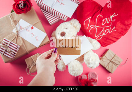 Buying presents for Valentines day with a gold card. Gift boxes and heart pillow on pink background Stock Photo
