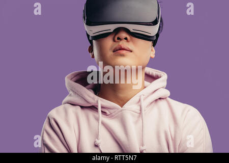 Asian young man dressed in white hoodie using virtual reality headset isolated over violet background Stock Photo