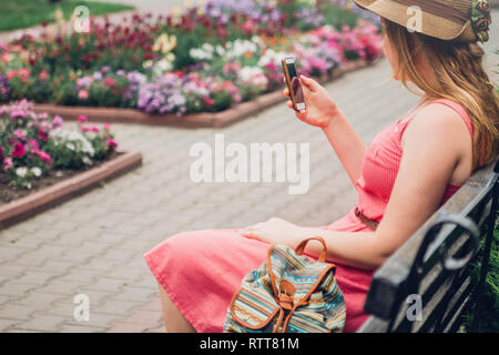 Teenager girl uses her phone in the park sitting on bench Stock Photo