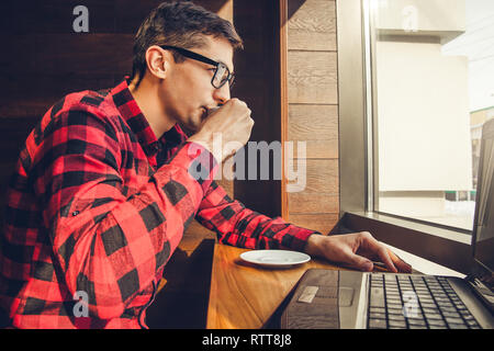 Young businessman enjoys coffee in the cafe talking on the phone and using a laptop in front of the window Stock Photo