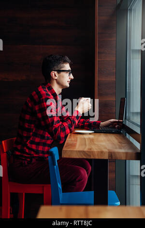 Young businessman enjoys coffee in the cafe talking on the phone and using a laptop in front of the window Stock Photo