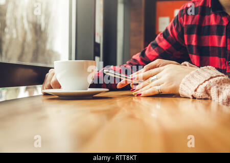 Young couple enjoys coffee in the cafe while using a smartphone in front of the window Stock Photo