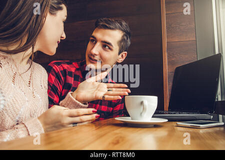 Young couple talks and enjoys coffee in the cafe using a laptop in front of the window Stock Photo