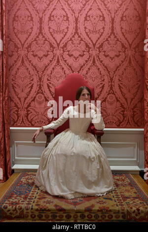 Queen Victoria sits on a throne at Kensington palace- the room is red and she wears a white dress Stock Photo