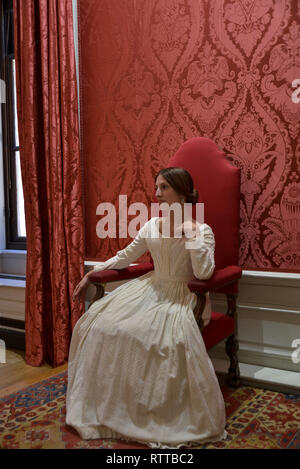 Queen Victoria sits on a throne at Kensington palace- the room is red and she wears a white dress Stock Photo