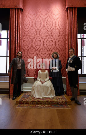 Queen Victoria sits on a throne at Kensington palace- the room is red and she wears a white dress, she is surrounded by 2 gentlemen & Baroness Lehzen Stock Photo