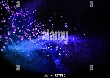 Split debris of purple stone exploding with blue dry river sand against black background. Stock Photo