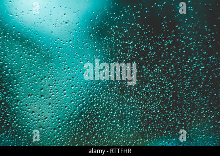 Water drops on windows close up against blurry dark teal background Stock Photo