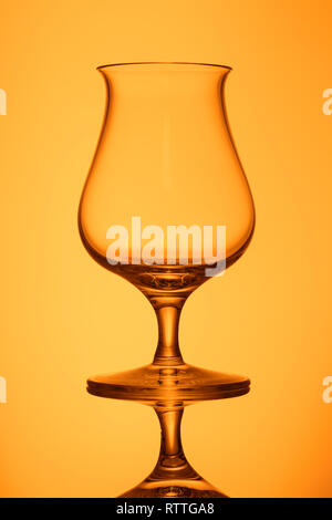 Lucid empty whisky glass in orange back lit vertical format Stock Photo