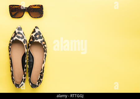 Sunglasses and trendy leopard print shoes on pastel yellow background, summer fashion concept. Top view, selective focus Stock Photo