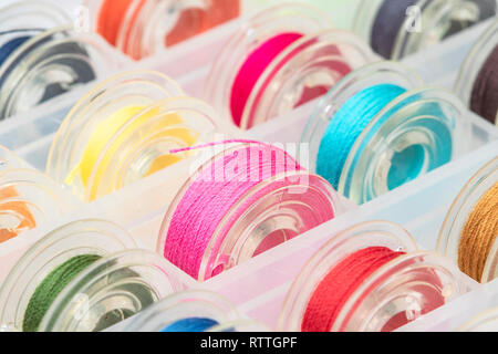 Close up plastic sewing machine bobbins with colourful thread in plastic box. Stock Photo