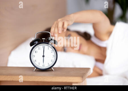 Young woman lying in bed, woken by alarm signal, turning off clock Stock Photo