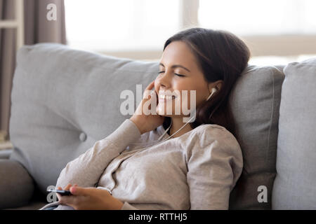 Smiling woman in earphones listening to music on phone at home Stock Photo