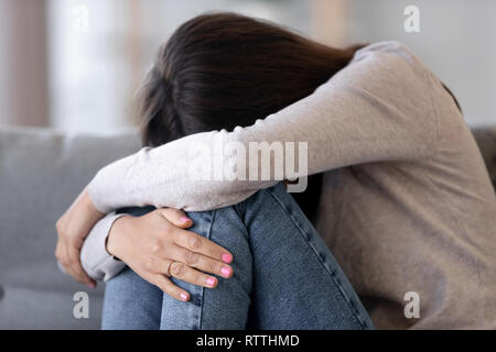 Upset young woman embracing knees, crying, feeling unhappy Stock Photo
