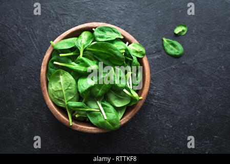 Baby spinach leaves in bowl on black background, top view, copy space. Clean eating, detox, diet food ingredient - green organic spinach. Stock Photo