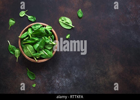 Baby spinach leaves in bowl on black background, top view, copy space. Clean eating, detox, diet food ingredient - green organic spinach. Stock Photo