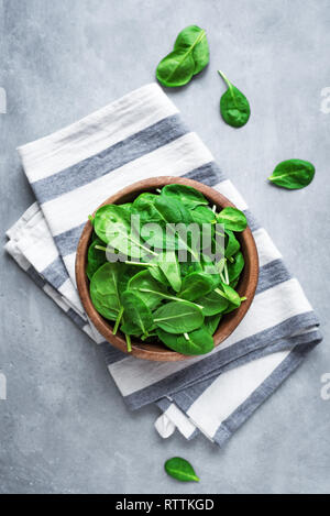 Baby spinach leaves in bowl on grey concrete background, top view, copy space. Clean eating, detox, diet food ingredient - green organic spinach. Stock Photo