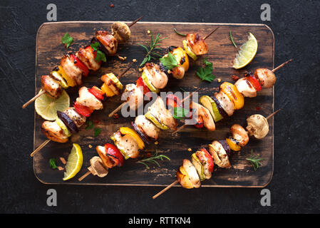 Grilled vegetable and chicken skewers with  bell peppers, zucchini, onion and mushrooms on black background, top view. Meat and vegetables kebabs on s Stock Photo