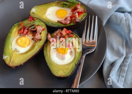 Quail eggs baked in avocado with bacon, red paprika and dill. Stock Photo