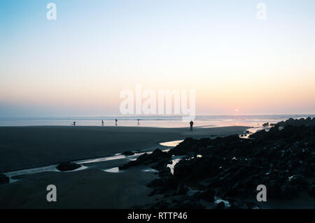 Surfers on the beach silhouetted at sunset on a warm February day. Saunton, Devon, 27th Feb 2019. Stock Photo