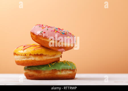 Three appetizing multi-colored donuts on a plain background of beige peach color. Copy space. The concept of serving sweets in the bakery. Hanukkah ba Stock Photo