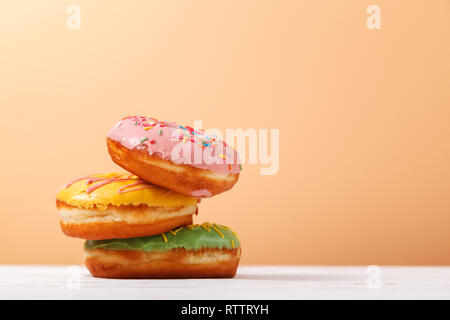 Three appetizing multi-colored donuts on a plain background of beige peach color. Copy space. The concept of serving sweets in the bakery. Hanukkah ba Stock Photo