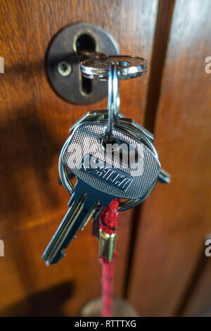 Close Up of Two metal keys hanging from a door key hole in wooden door