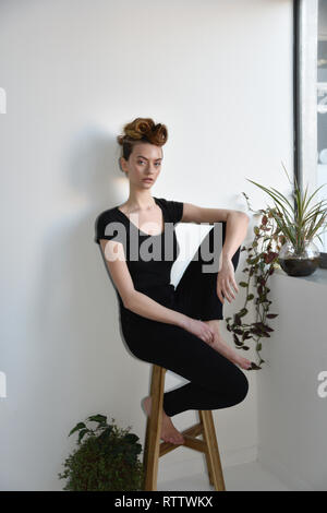 A beautiful High Fashion Model poses in a predominantly white space and is wearing black jeans and a t shirt. She has her hair up and is very cool Stock Photo