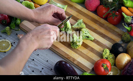Man is cutting vegetables in the kitchen, slicing broccoli Stock Photo