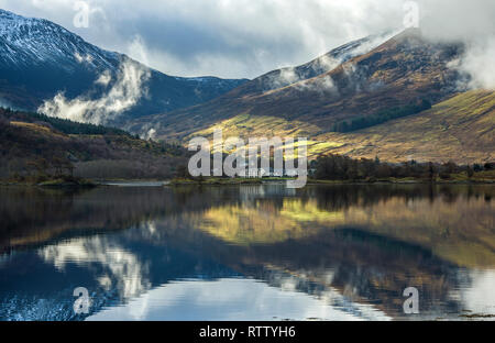 Clear reflections of the mountains and trees on Loch Leven, Glencoe, on a beautifully lit winter day in February. Stock Photo