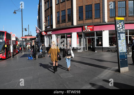 Rear view of women walking past KFC Kentucky Fried Chicken restaurant on Brixton Road in Brixton, Borough of Lambeth, South London UK   KATHY DEWITT Stock Photo