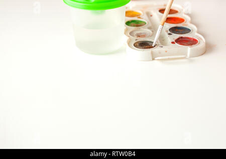Set of watercolor paints and paintbrushes for painting on white background closeup, copy space. Selective focus. Stock Photo