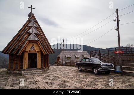 St. Sava wooden serb orthodox church and an old Volga Soviet car next to it in Drvengrad ethno village built by Emir Kusturica for his film. Serbia Stock Photo