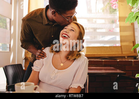African man with his girlfriend, kissing on her forehead standing in coffee shop. Happy couple on date at coffee shop.