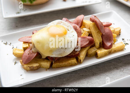 Salchipapas made of French fries and fried sausage, traditional fast food in South America, served on plates, mayonnaise, mustard and ketchup Stock Photo