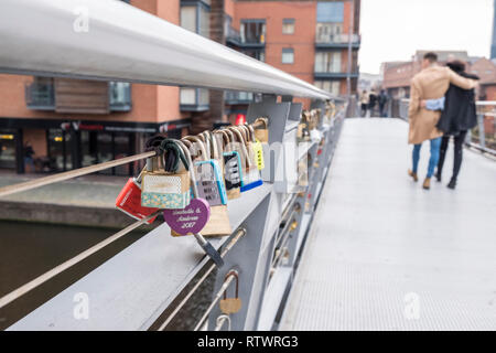 Embracing couple walk past Lovelocks or love locks padlocked on to a bridge in Birmingham, England, GB, UK. Stock Photo