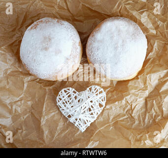 Two sugared donuts decorated with a white heart in the brown baking paper top view, funny cooking concept Stock Photo