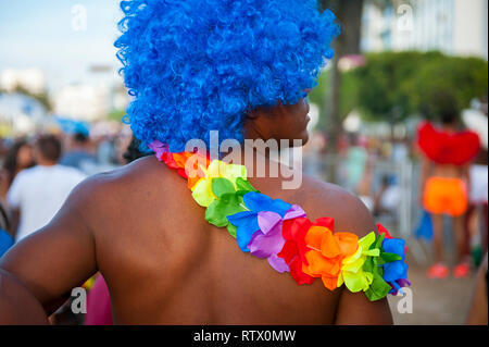 Close up of brightly colored rainbow flower lei and blue afro wig on an unrecognizable man at a Brazilian Carnival street party in Rio de Janeiro Stock Photo