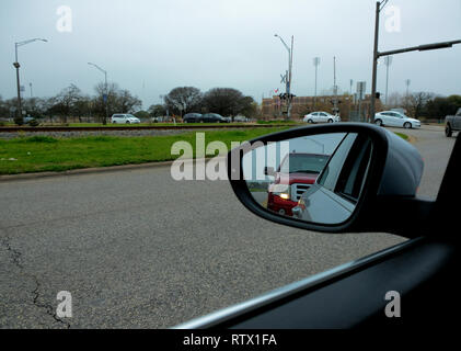 Side view mirror on an overcast day in Texas; reflection of red car in rear at a stop light. Stock Photo