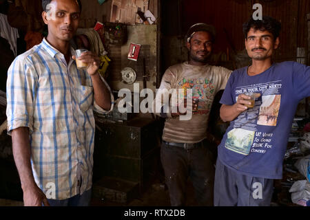 Employees in a small and dingy workshop in Mumbai, India, having a tea break drinking masala tea, i.e. tea with milk and spices Stock Photo