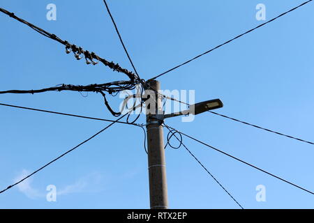 Concrete electrical utility pole with modern LED public light and multiple electrical wires going in all directions on clear blue sky background Stock Photo