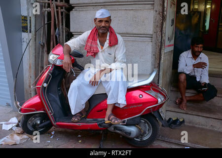 A handcart puller in Kalbadevi Rd., Mumbai, India, an ethnic Maharashtrian, resting on a motor scooter, its color coincidentally matching his scarf's Stock Photo