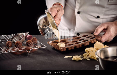 Chef or chocolatier pouring melted white chocolate into silicone molds from a saucepan in a close up on his hands